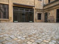 an outdoor courtyard has brick paving and windows with several bicycles parked in it's corner