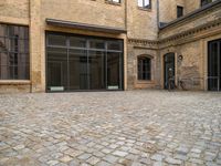 an outdoor courtyard has brick paving and windows with several bicycles parked in it's corner