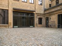 an outdoor courtyard has brick paving and windows with several bicycles parked in it's corner