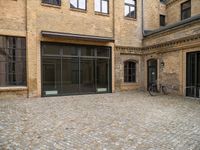 an outdoor courtyard has brick paving and windows with several bicycles parked in it's corner