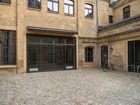 an outdoor courtyard has brick paving and windows with several bicycles parked in it's corner