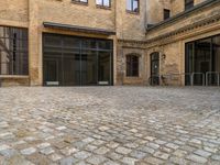 an empty brick courtyard with a parking spot for bikes in the foreground and glass windows on the side