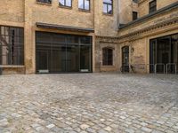 an empty brick courtyard with a parking spot for bikes in the foreground and glass windows on the side