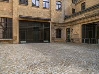 an empty brick courtyard with a parking spot for bikes in the foreground and glass windows on the side