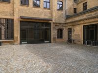 an empty brick courtyard with a parking spot for bikes in the foreground and glass windows on the side