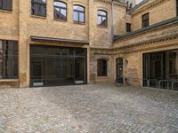 an empty brick courtyard with a parking spot for bikes in the foreground and glass windows on the side