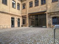 a brick sidewalk with lots of windows in it, near a bike rack and a few bicycles parked in it