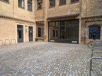 a brick sidewalk with lots of windows in it, near a bike rack and a few bicycles parked in it