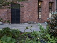 a fire hydrant is in front of a red brick building and shrubs around it