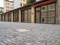 a brick pavement near two building with metal windows and red rails on top and glass walls