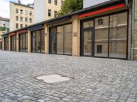 a brick pavement near two building with metal windows and red rails on top and glass walls