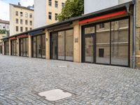 a brick pavement near two building with metal windows and red rails on top and glass walls