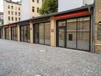 a brick pavement near two building with metal windows and red rails on top and glass walls