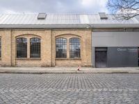 two brown brick buildings with arched windows on the front of each building, on cobblestones