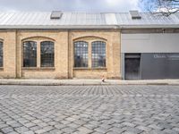 two brown brick buildings with arched windows on the front of each building, on cobblestones