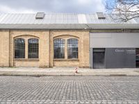 two brown brick buildings with arched windows on the front of each building, on cobblestones