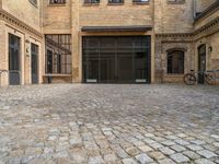 a cobblestone courtyard with a bicycle leaned up against a rail near a brick building