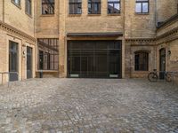 a cobblestone courtyard with a bicycle leaned up against a rail near a brick building