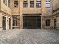 a cobblestone courtyard with a bicycle leaned up against a rail near a brick building