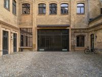 a cobblestone courtyard with a bicycle leaned up against a rail near a brick building