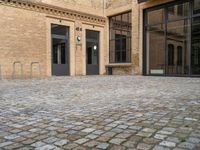 two doors of a building in a courtyard next to a fence and a bench on the side of a brick road