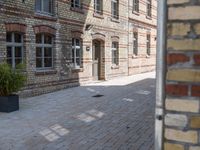 a clock on a brick wall by a sidewalk outside a building that is being used for landscaping