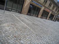 the sidewalk is paved with stones and has a bench in front of it, with no people inside