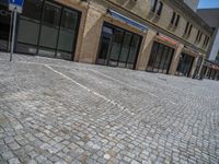 the sidewalk is paved with stones and has a bench in front of it, with no people inside