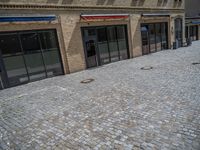 the sidewalk is paved with stones and has a bench in front of it, with no people inside