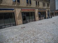 the sidewalk is paved with stones and has a bench in front of it, with no people inside