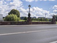 the bridge crosses over a busy highway and there is an ornamentally decorated fence with statues