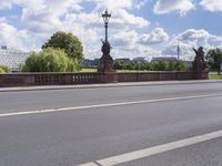 the bridge crosses over a busy highway and there is an ornamentally decorated fence with statues