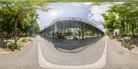 a fisheye view of a bridge and roadway near trees and parked cars on both sides