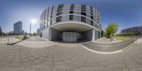 a building with a circular view of a parking garage and stairs going into it and a man riding a bike down the sidewalk