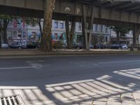 the shadow of a train bridge over a street with cars in the background and trees on both sides