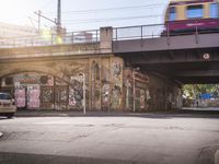 a bus going under a bridge near a road full of graffiti and graffiti art on the wall