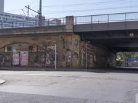 a bus going under a bridge near a road full of graffiti and graffiti art on the wall