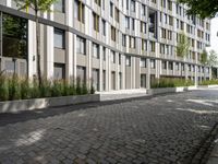 a very nice sidewalk leading to a tall building with many windows and some bushes around