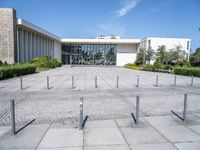 an empty parking lot with lots of poles on each side of the building and large glass windows in the back