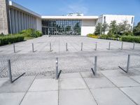 an empty parking lot with lots of poles on each side of the building and large glass windows in the back