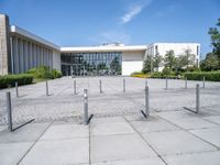 an empty parking lot with lots of poles on each side of the building and large glass windows in the back