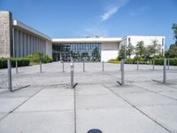 an empty parking lot with lots of poles on each side of the building and large glass windows in the back