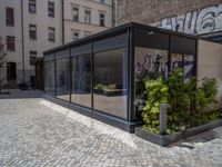 several plants sit in decorative concrete planters along the sidewalk of a building that is very modern