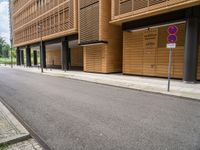 an empty street and an intersection sign in front of brown building with black windows on both sides