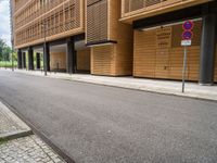 an empty street and an intersection sign in front of brown building with black windows on both sides