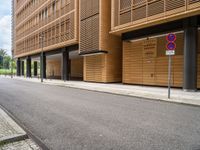 an empty street and an intersection sign in front of brown building with black windows on both sides