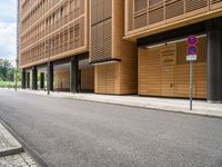 an empty street and an intersection sign in front of brown building with black windows on both sides