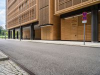 an empty street and an intersection sign in front of brown building with black windows on both sides