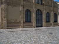 the sidewalk is paved with stones and has a bench in front of it, with no people inside