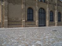 the sidewalk is paved with stones and has a bench in front of it, with no people inside